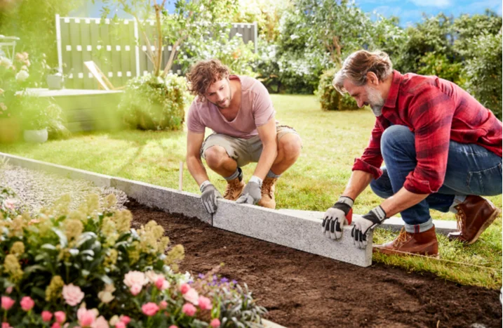 Zwei Personen verlegen Randsteine im Garten.